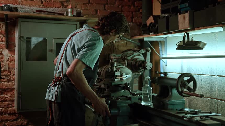 Man operates a metal lathe in a workshop with exposed brick walls