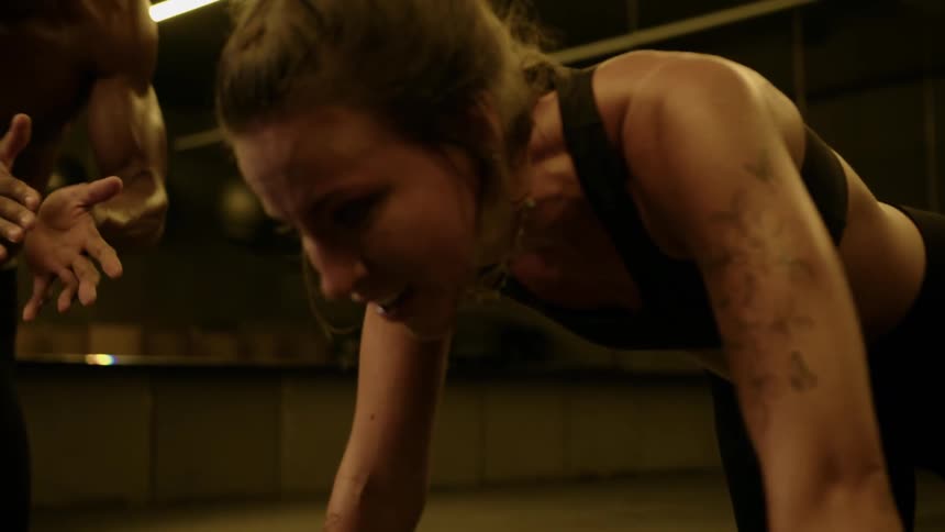 A determined woman with a strained expression and visible sweat is intensely focused on a physical activity with another persons partially visible in the foreground