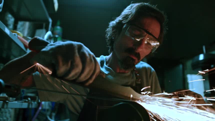 A focused male worker wearing safety glasses is actively grinding metal creating a brilliant shower of sparks in a dimly lit workshop environment