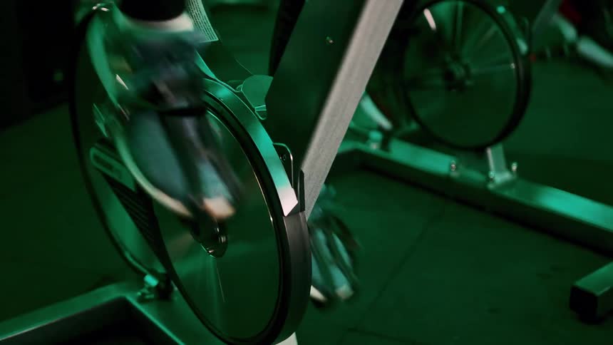 Two people riding stationary exercise bikes in a lowlight environment