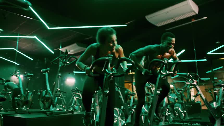 A man and a woman are cycling in the gym