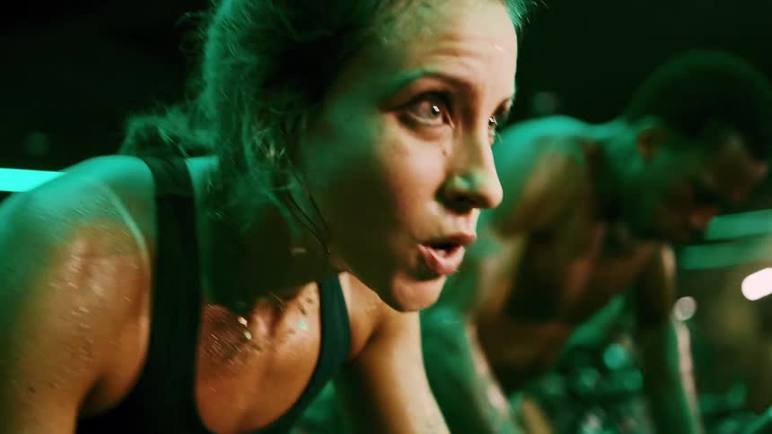 A woman and a man are intensely focused and dripping with sweat powers through a workout under neon lights