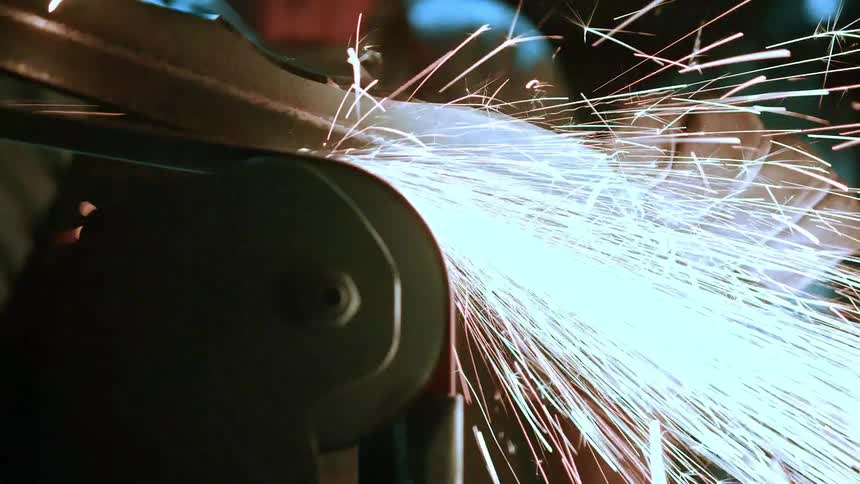 A dynamic closeup captures a metal grinding process with a large shower of bright sparks erupting from the point of contact