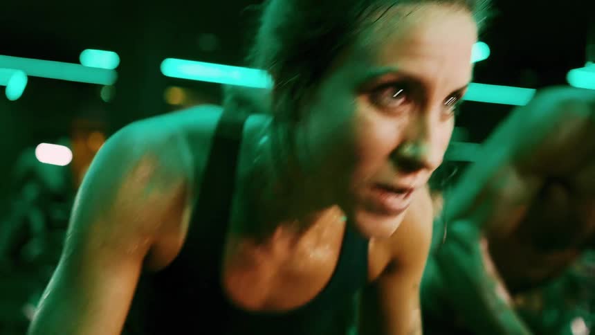 A woman and a young man cycle on stationary bikes in the gym sweating