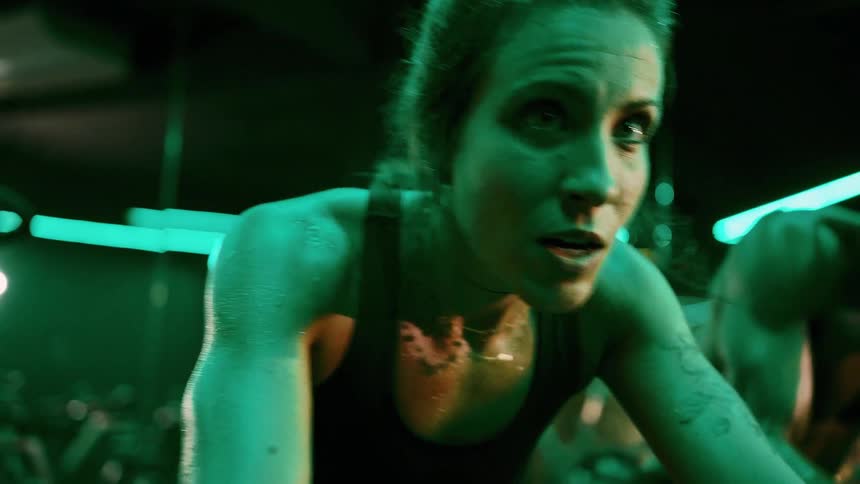 A woman and a young man cycle on stationary bikes in the gym sweating