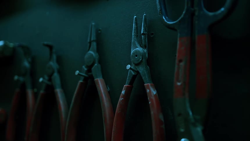 A row of wellused pliers and tools hang neatly on a dark workshop wall