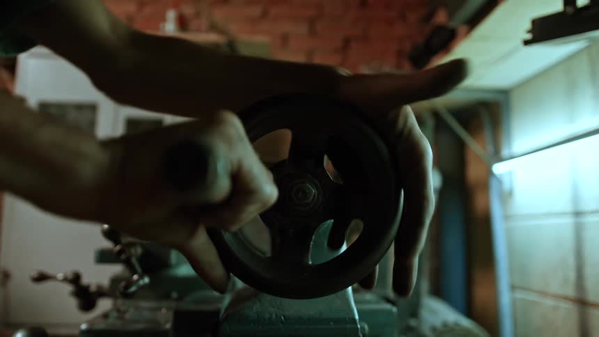 Man turns the wheel on a machine while working in a workshop