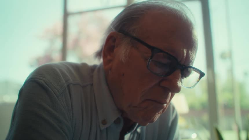 Close up portrait of an elderly man focused on a task while seated in a room during daytime