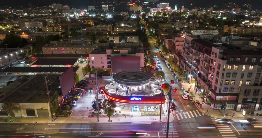 Night aerial view of a busy avenue with the circular Tesla Diner restaurant brightly lit surrounded by residential and commercial buildings