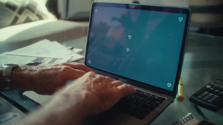 An elderly man types on the keyboard of a laptop computer