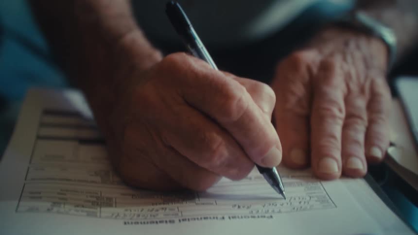 Close up of an elderly man filling up a financial form on a table in a living room