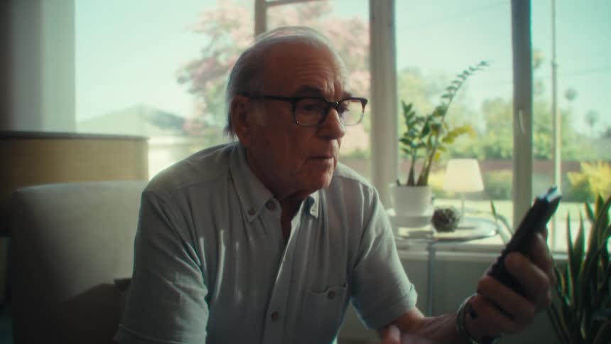 Elderly man sitting indoors and interacting with a smartphone