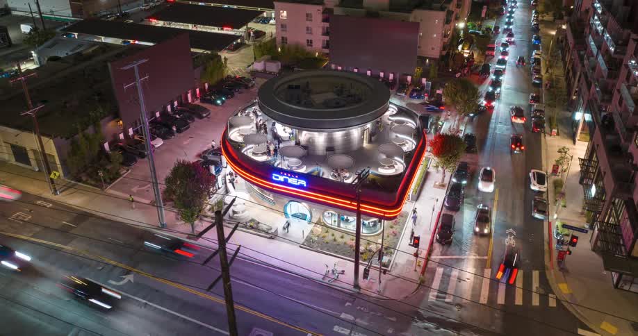 A retrostyle Tesla Diner glows brightly at night as cars and pedestrians fill the surrounding city streets