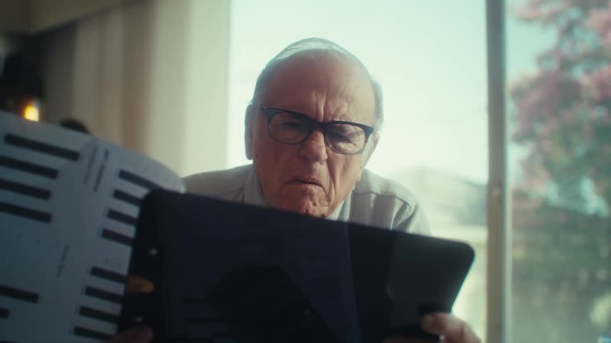 Close up of an elderly man contemplating after going through paper documents on a clipboard while sitting in a room during daytime