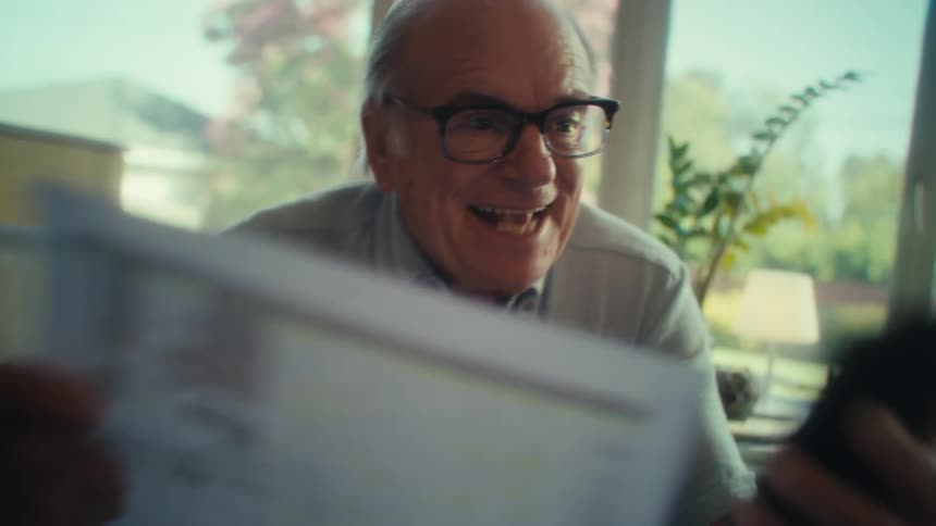 An elderly man celebrates after checking calculations on a paper document in a room during daytime