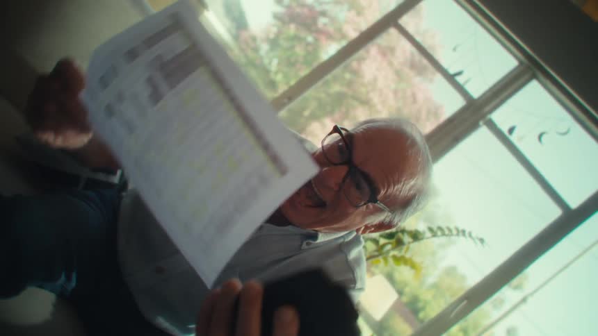 Man cheers while reading a paper and his cell phone