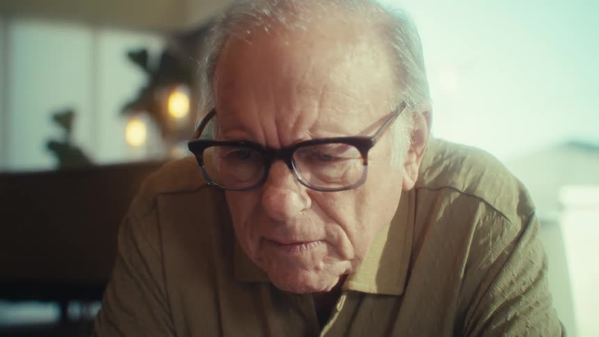 Close up of an elderly man smiling while using a laptop in a room during daytime
