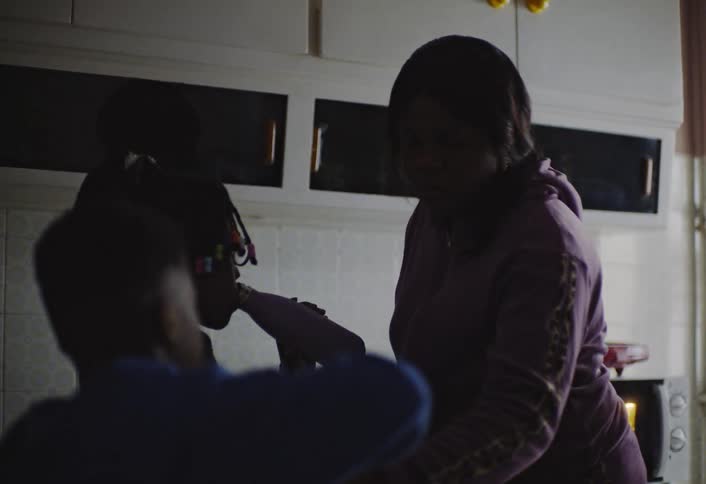 A black mother collects a water bottle from her son and drops it on the kitchen counter as she prepares her children for the day