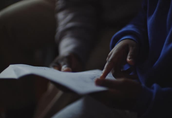 Child points to a paper with notes while receiving help from an adult