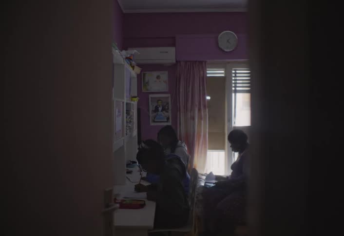 Children study in a bedroom while a woman helps one of them with a notebook