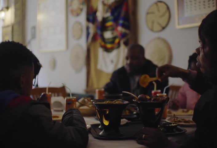 A family gathered around a table in a restaurant or dining room eating from various dishes while conversing with decorative items on the wall in the background