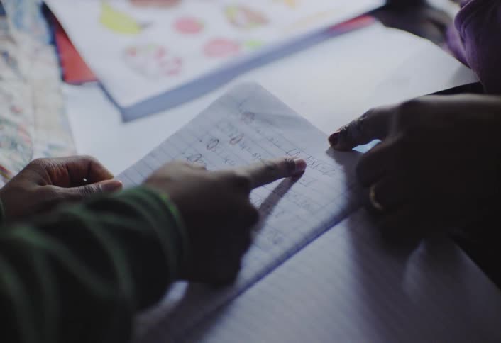 Two hands of an adult and a child interacting with an open notebook