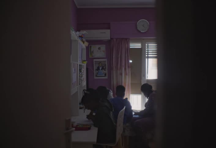 An adult walks into a room children are seated looking down at books doing homework on a bedroom