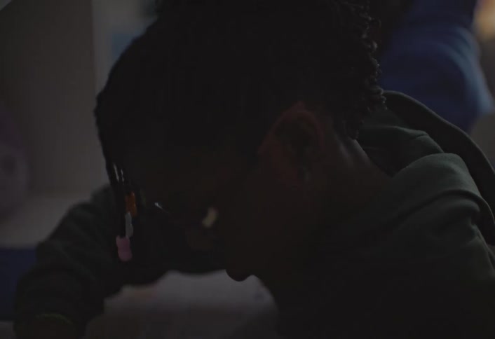 Three siblings sit behind a desk doing their homework and writing while their mother checks their work