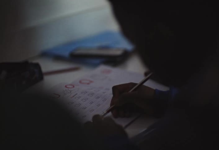 A child partially silhouetted in low light concentrates on writing at a desk