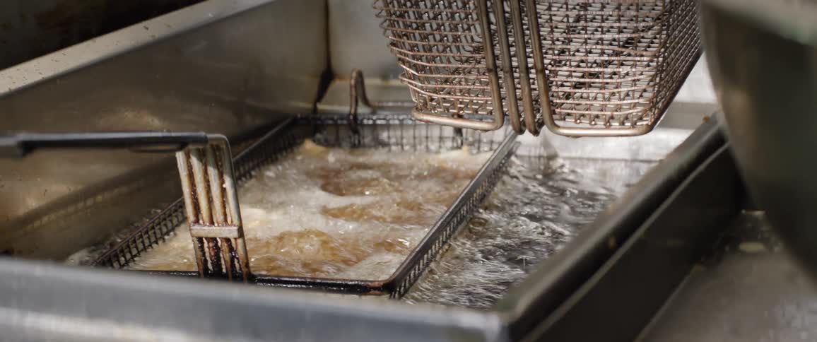 The video shows two deep fryers filled with bubbling hot oil with metal baskets submerged in them in the left fryer fried food is visible submerged in the oil while the right basket is empty and raised above the oil the camera pans slightly revealin