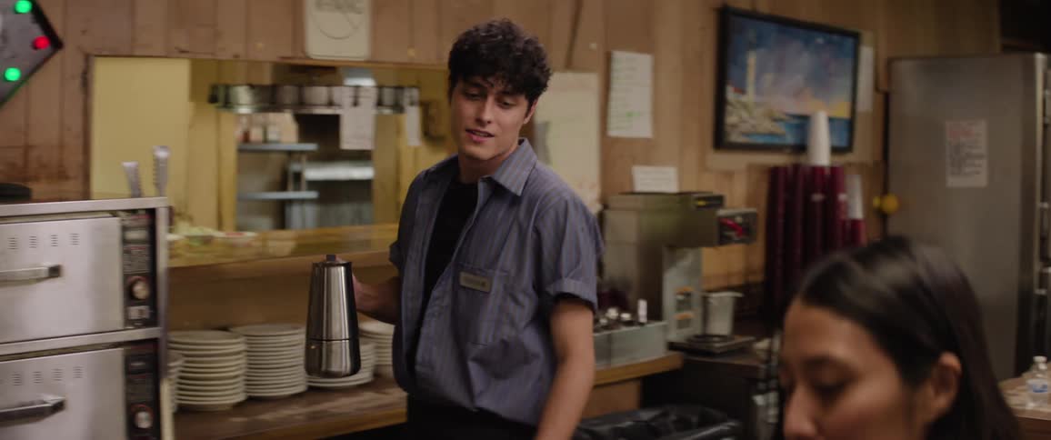 A waiter serves a woman coffee inside a restaurant with a smile on his face