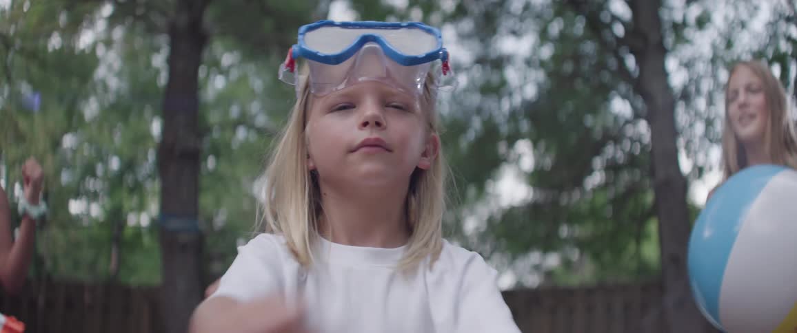 Children in a backyard playing with a little blonde girl warming her arms