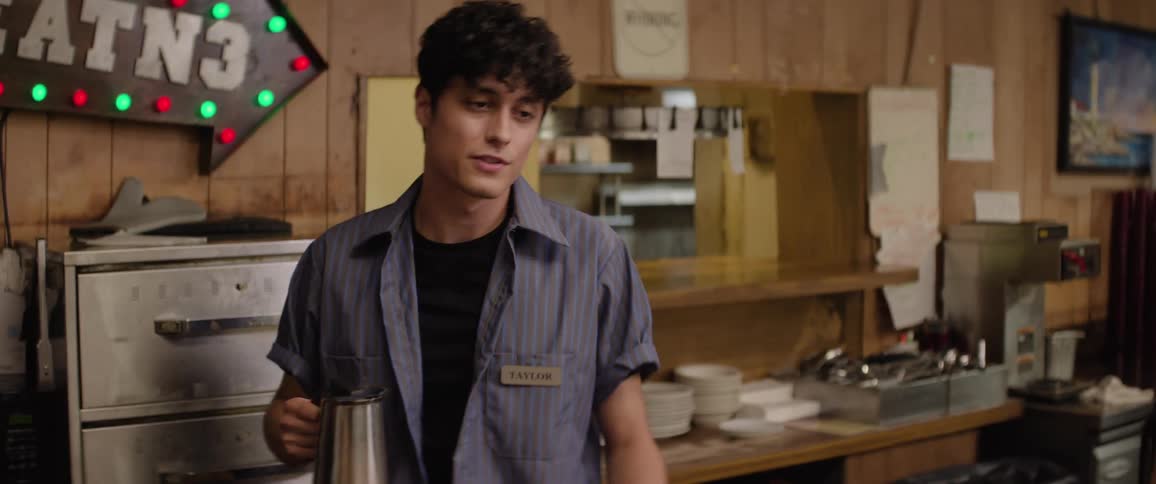 A waiter serves a woman coffee inside a restaurant with a smile on his face