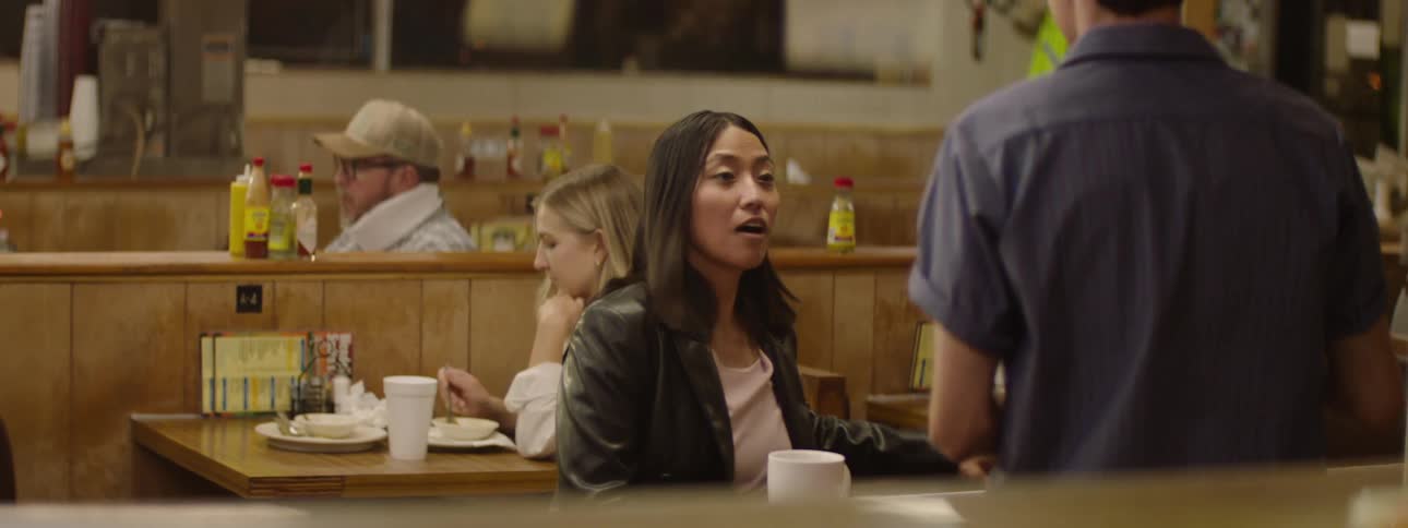 Female customer sits at the counter in a restaurant during the evening and greets the waiter