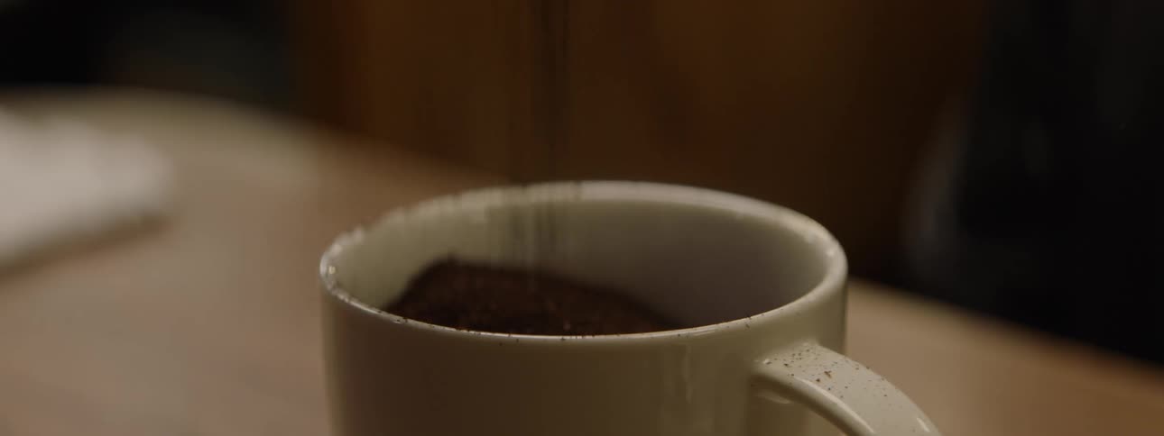 Dark ground coffee is gradually poured directly into a ceramic mug
