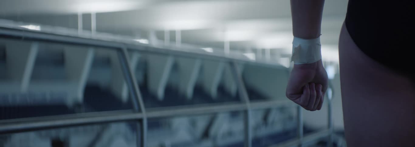 A close view of a persons arm and hand wearing a white wristband hangs down with a light blurred background of what appears to be part of a swimming facility