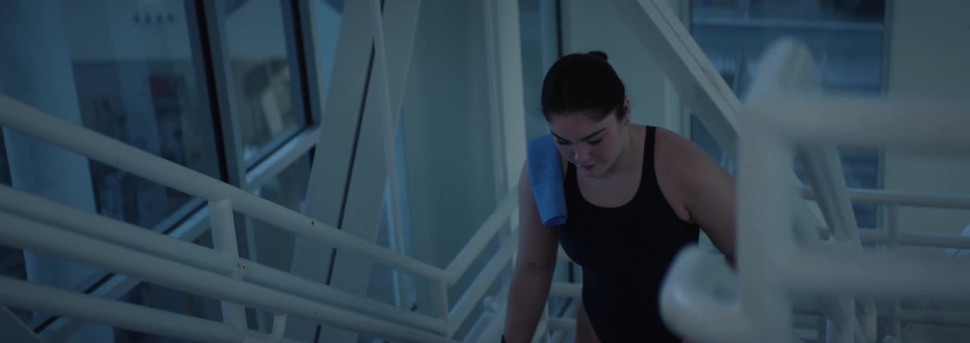 Woman with tied hair and a black swimsuit walking up the stairs of an indoor space