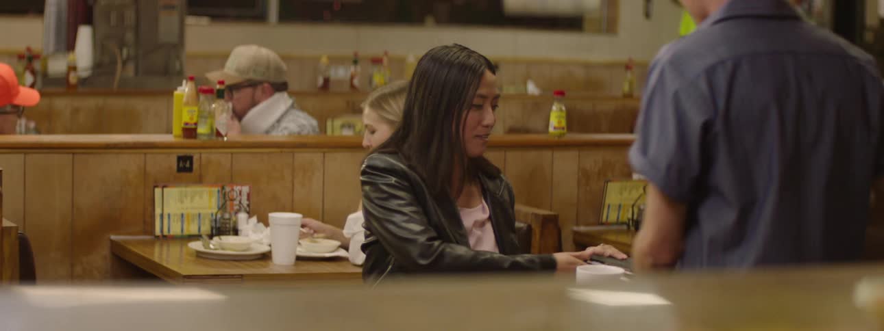 Woman sitting in a coffee shop and being served by a man