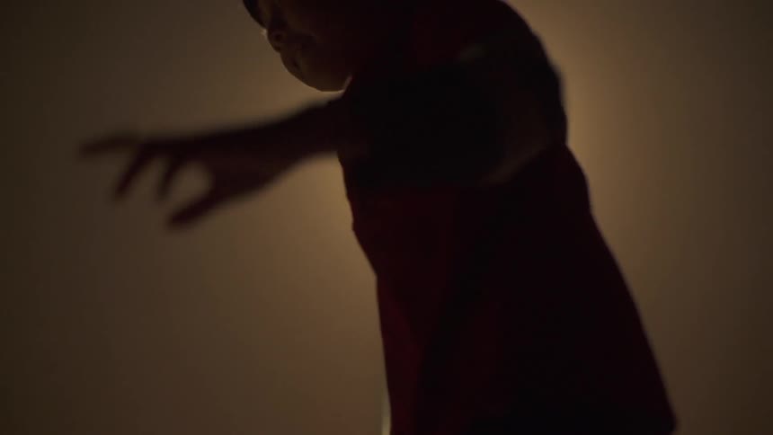 A silhouette of an asian child tries to stand in balance in the spotlight