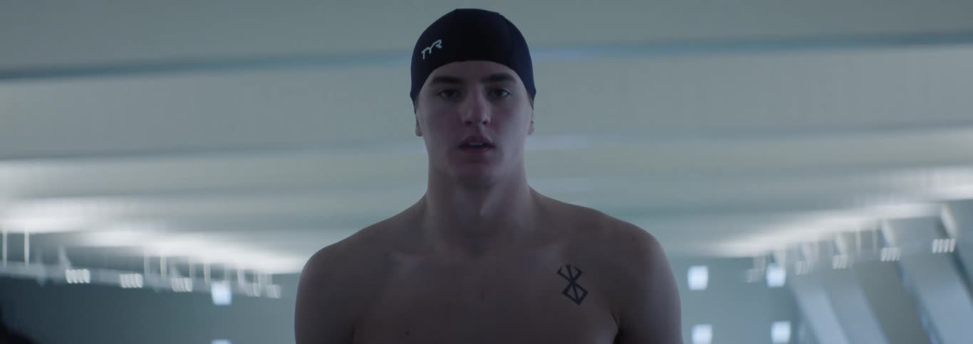 The video shows a swimmer wearing a black swim cap with a white tyr logo on the front the swimmer is seen from the chest up looking downwards and has a tattoo on their right shoulder
