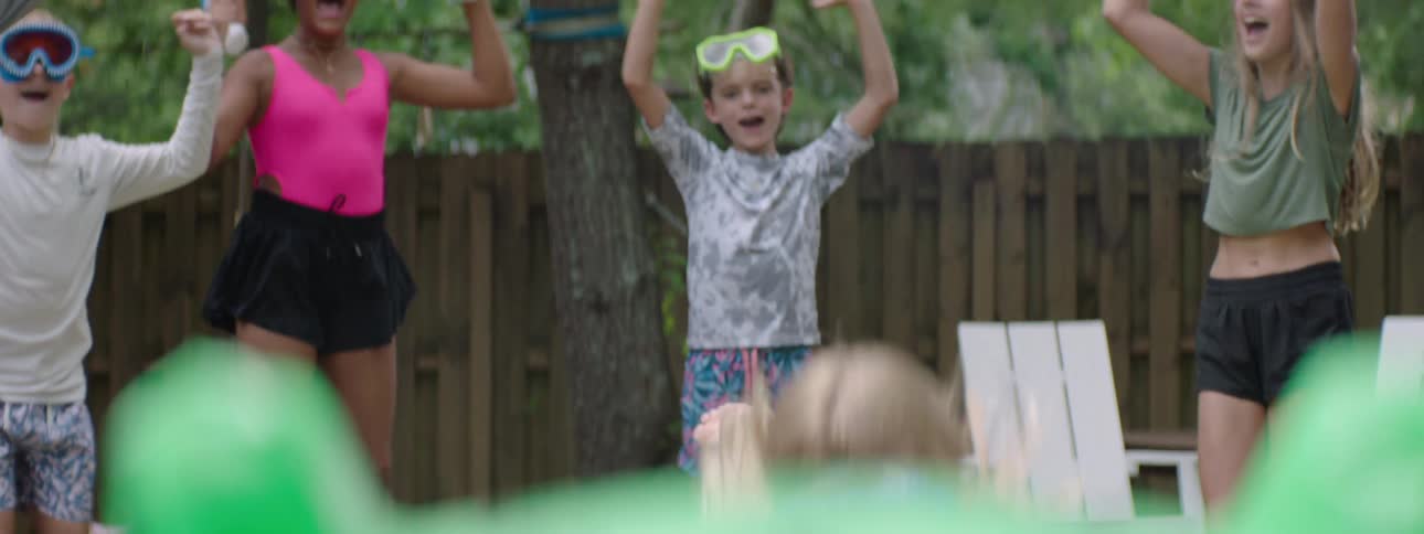 Children jumping in a yard happily and watching a little girl running and playing