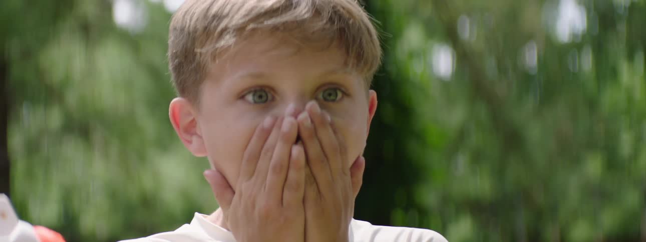 The video shows a young boy with short light brown hair looking directly at the camera his eyes widen and his mouth opens in an expression of surprise or awe