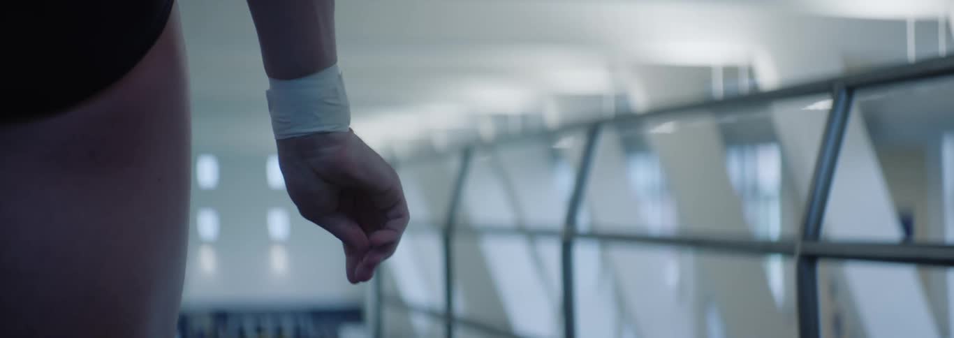 A close view of a persons hand and forearm wearing a white wristband is clenched into a fist moving slightly against a blurred light background of a large indoor facility