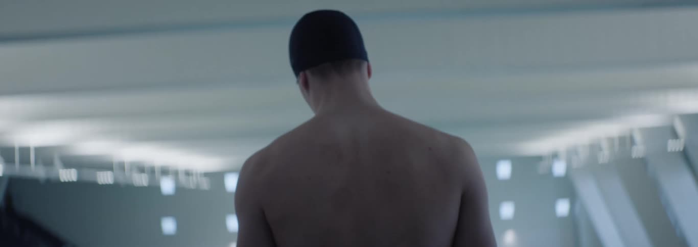 A man wearing a bathing cap walks in the frame and he also looks depressed