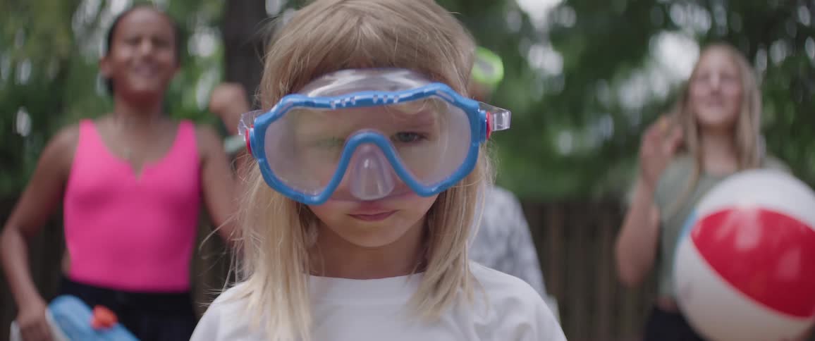 Kids at a pool party cheer for a young girl as she puts on her swimming goggles in preparation for a swim