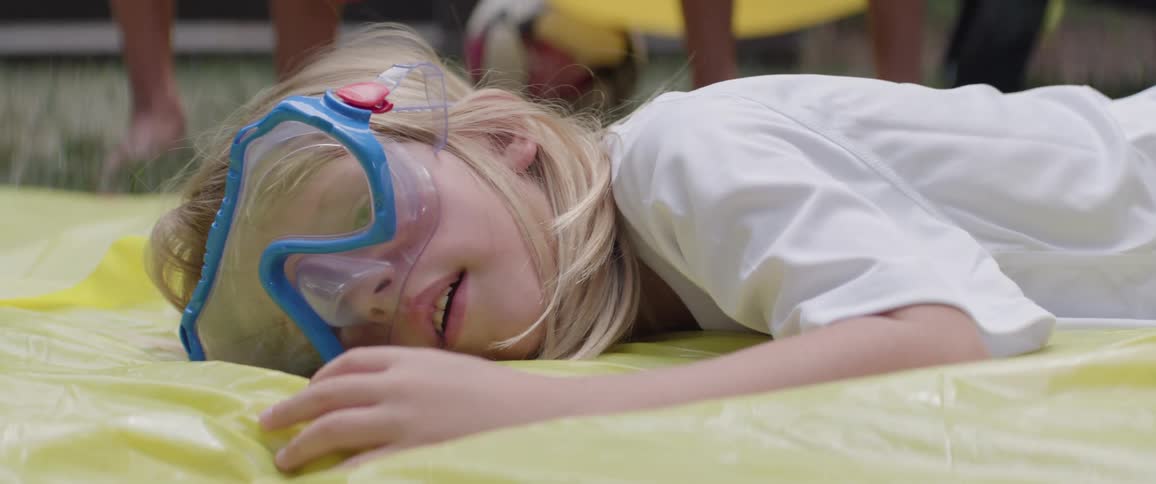 Little blonde girl falling on an inflatable tarp in a backyard