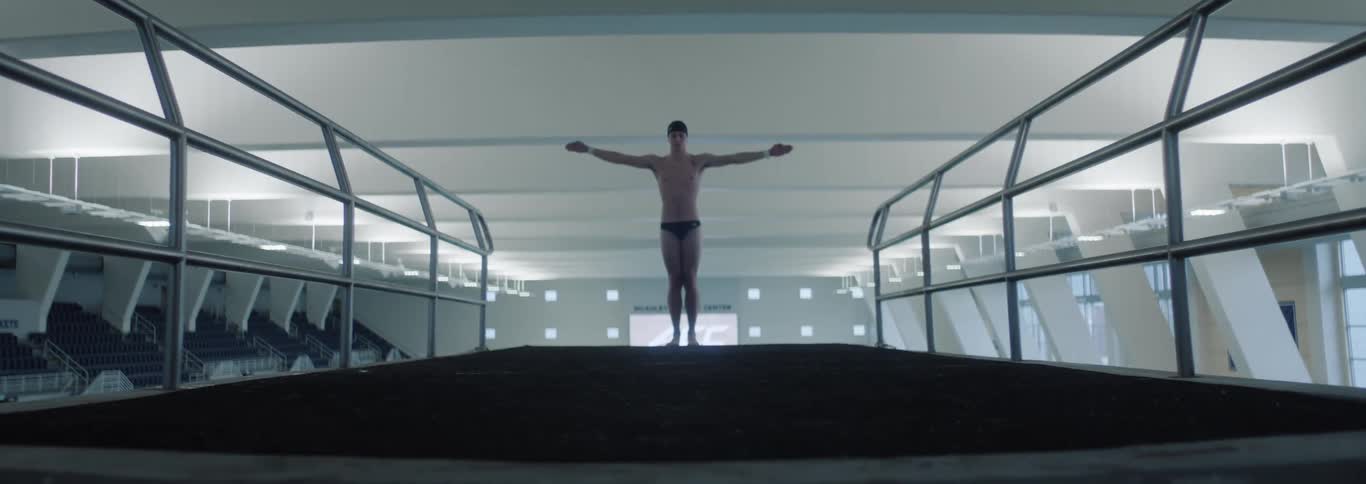 Man in swim trunks with open arms in an indoor environment
