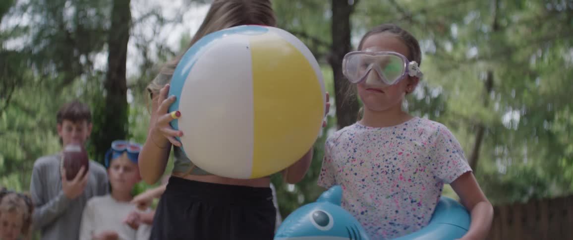 Children holding toys in an outdoor setting in a yard with trees and with disbelieving facial expressions