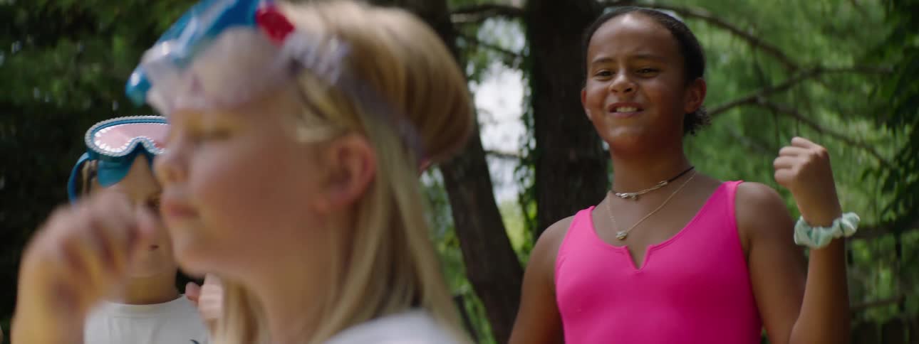 Little blonde girl with her eyes closed concentrating and in the background other children cheering happily in a backyard