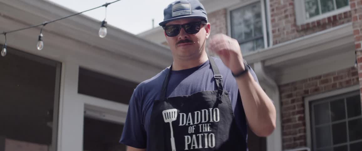 Barbecue chef holding a spatula and wearing an apron taking off his glasses